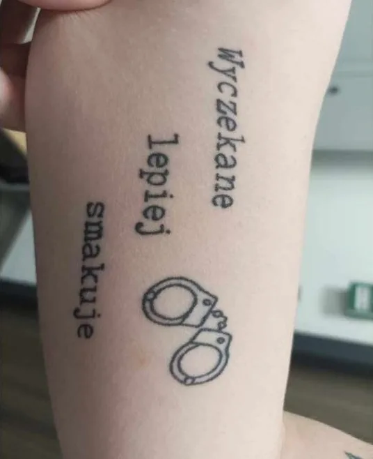Napis z kajdankami na przedramieniu — fine line lettering